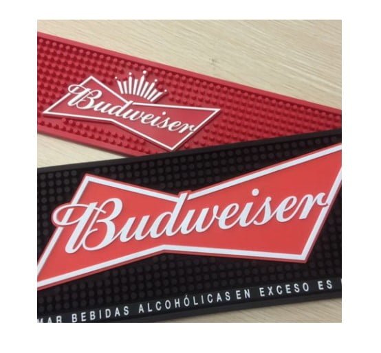 Two "The Bar Runner" mats, one red and one black with the Budweiser logo in white script, are set on a light wooden surface.