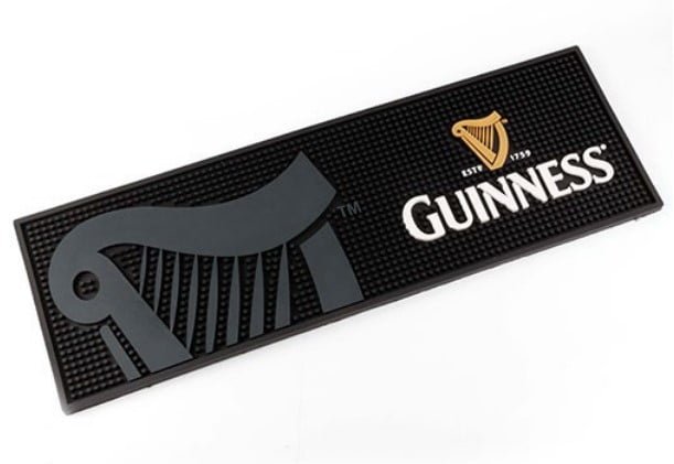 The Soft Rubber Bar Mat (Bar Rail) is a rectangular black mat with a gray harp on the left and the Guinness logo—gold harp and white text—on the right.