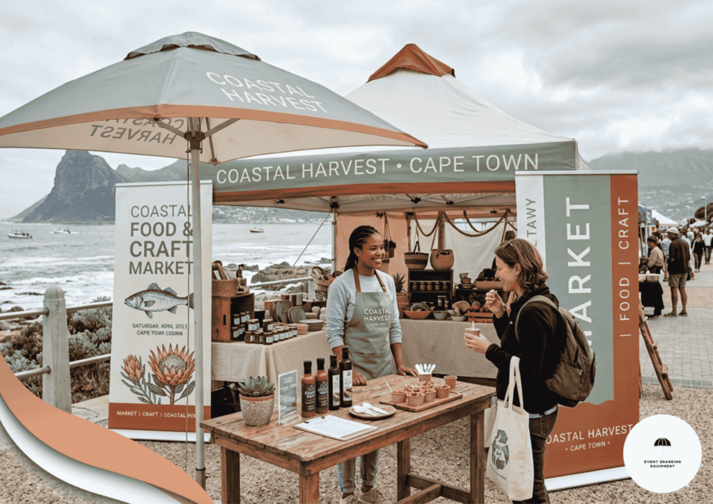 Two women interact at an outdoor market stall labeled "Coastal Harvest Cape Town," with food products displayed and a coastal landscape in the background.